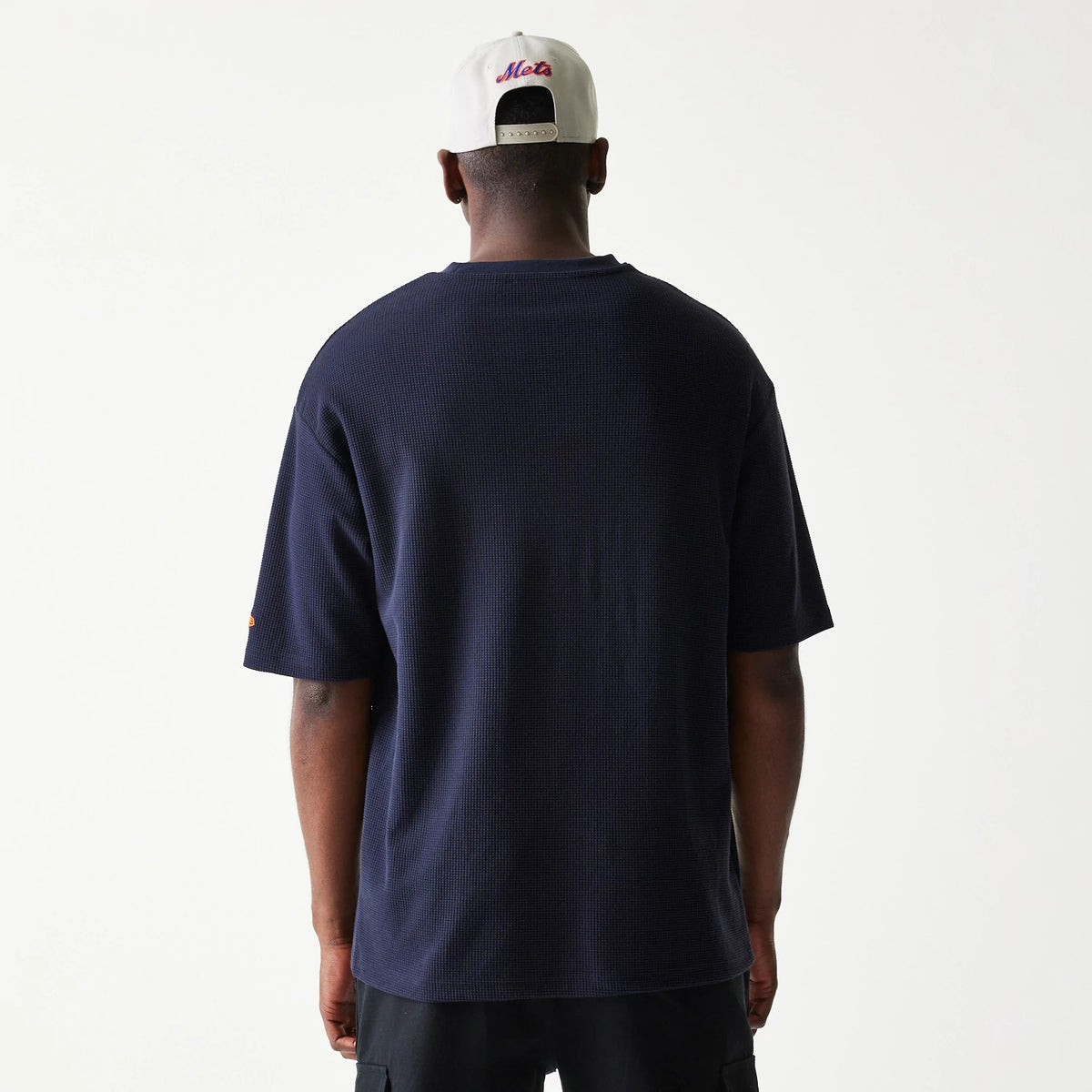 New Era New York Mets MLB Waffle Navy Oversized T-Shirt, back view on a model paired with a white cap, showing the plain navy fabric with a relaxed fit and short sleeves, enhancing the casual silhouette.