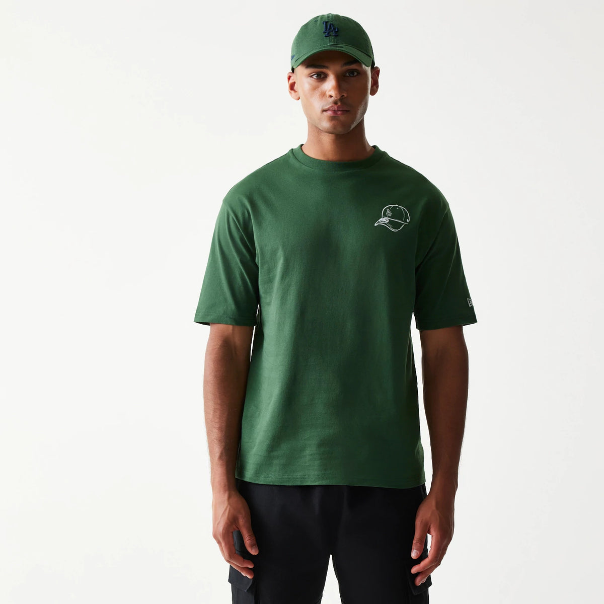 New Era LA Dodgers MLB Baseball Graphic Dark Green Oversized T-Shirt, front view on-model showing the outline graphic of a cap on the left chest, short sleeves, and the embroidered New Era logo on the lower right sleeve.