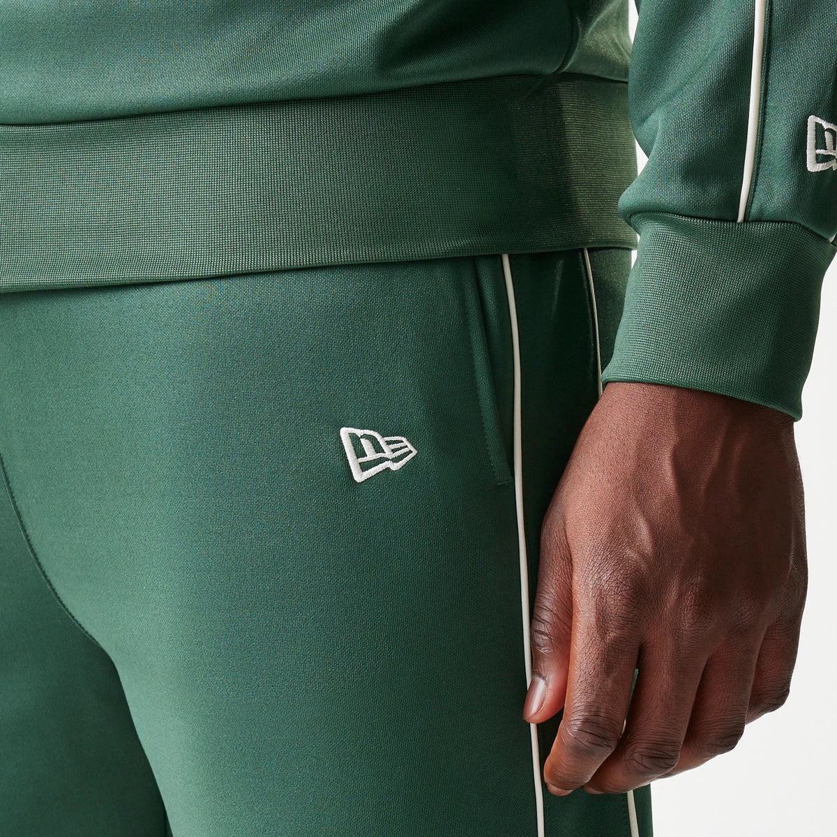 New Era LA Dodgers MLB Piping Dark Green Straight Leg Joggers, close-up view showing the white New Era flag logo embroidered near the pocket, with white piping running down the side seams and a ribbed waistband.