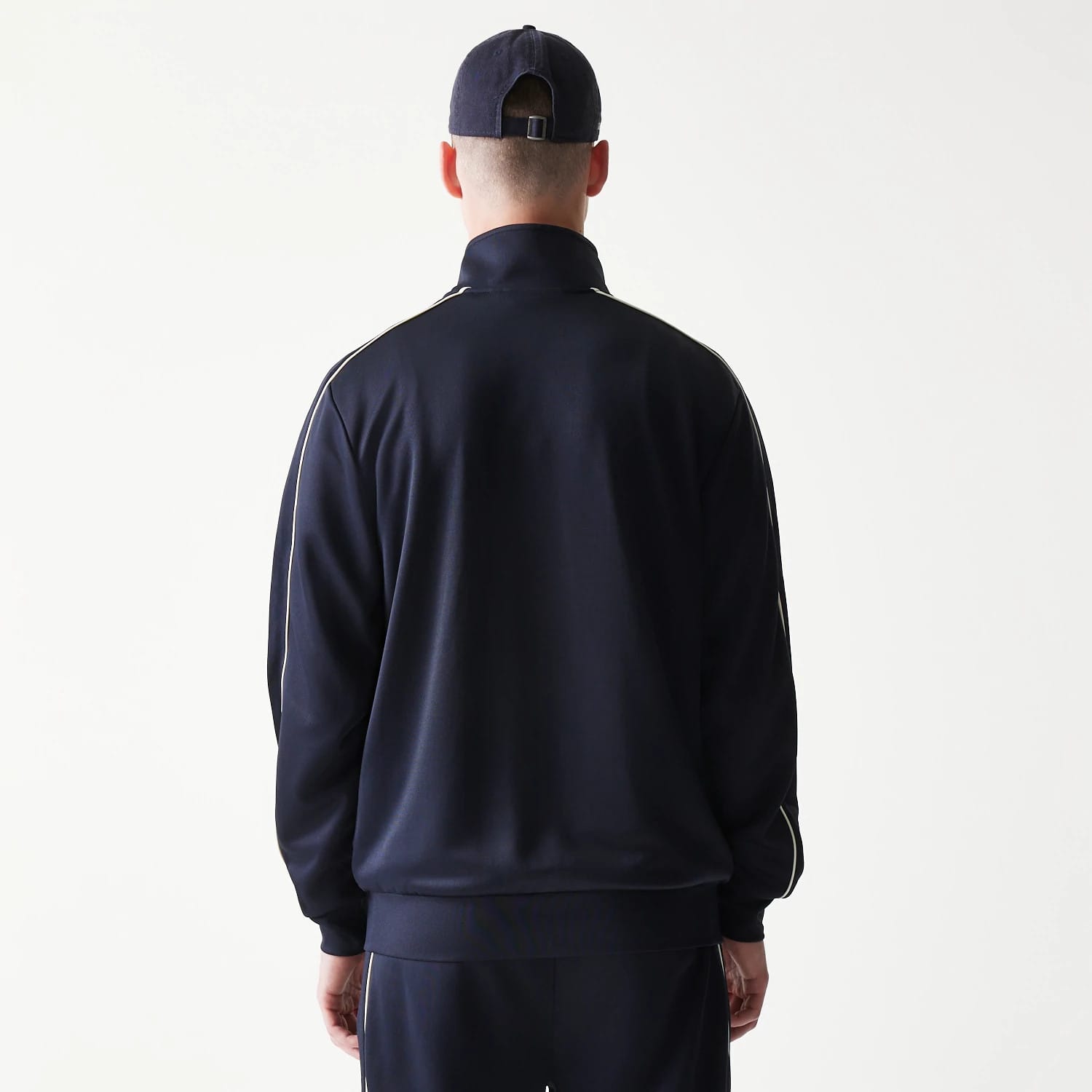 New Era New York Yankees MLB Piping Navy Track Jacket, back view showing the plain navy back with white piping along the shoulders and sleeves on a model wearing a matching navy cap.