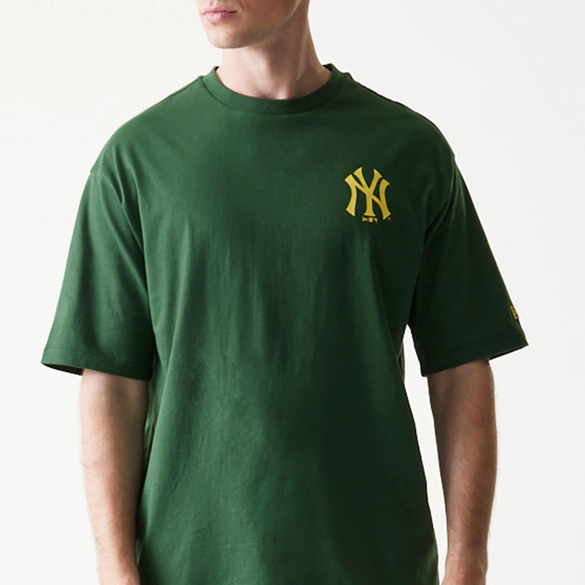 New Era New York Yankees MLB World Series Dark Green T-Shirt, front view on-model showing a dark green T-shirt with a yellow printed New York Yankees logo on the left chest and a yellow New Era logo on the sleeve.