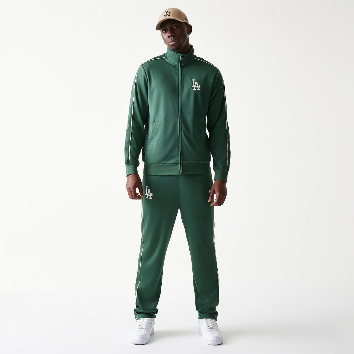 New Era LA Dodgers MLB Piping Dark Green Track Jacket, front view on-model wearing a matching cap, featuring a white embroidered LA logo on the left chest and piping along the shoulders and sleeves, creating a athletic look.