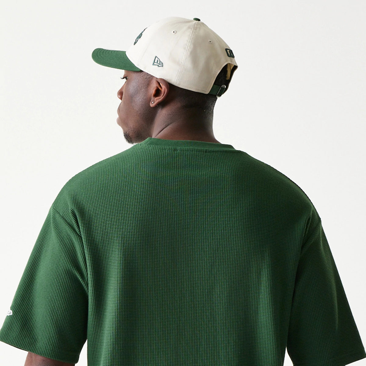 New Era LA Dodgers MLB Waffle Dark Green Oversized T-Shirt, back view on-model showing the textured dark green fabric extending across the shoulders, with a small embroidered New Era logo on the sleeve and paired with a two-tone cap.