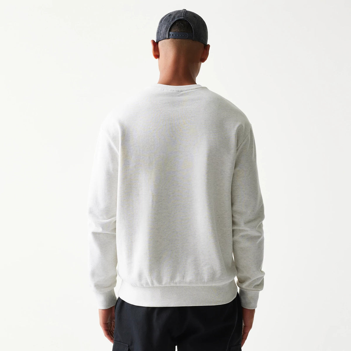 New Era New York Yankees MLB Graphic Pastel Grey Oversized Crew Neck Sweater, back view on a model wearing a dark cap and black trousers, showing a simple grey design with ribbed cuffs and hem.