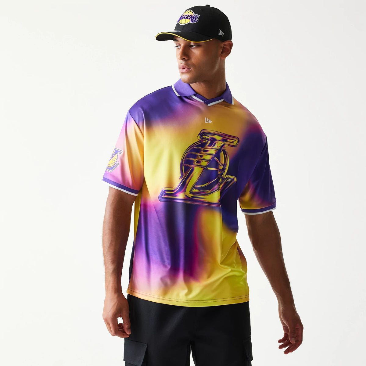 New Era LA Lakers NBA All Over Print Purple T-Shirt, front view on-model showing a blend of purple and yellow with a large debossed Lakers logo on the chest, NBA logo patch on the left sleeve and a small printed New Era logo near the collar.