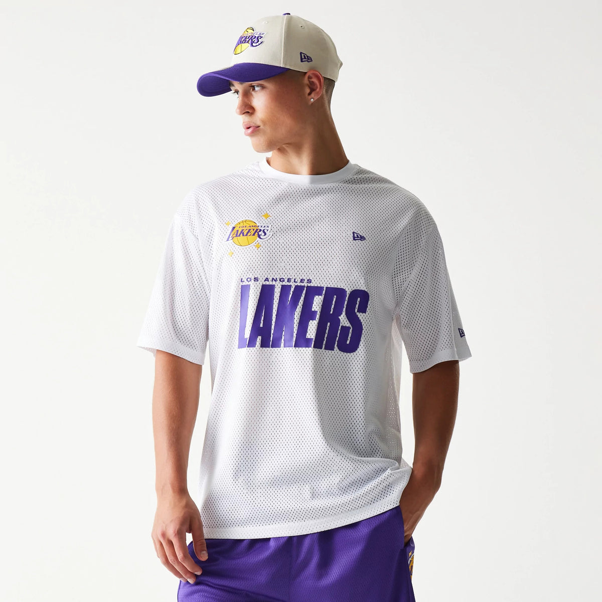 New Era LA Lakers NBA Graphic Mesh White T-Shirt, front view on-model showing large purple Lakers lettering across the chest, a printed team logo to the left, and a small embroidered New Era logo on the right shoulder.