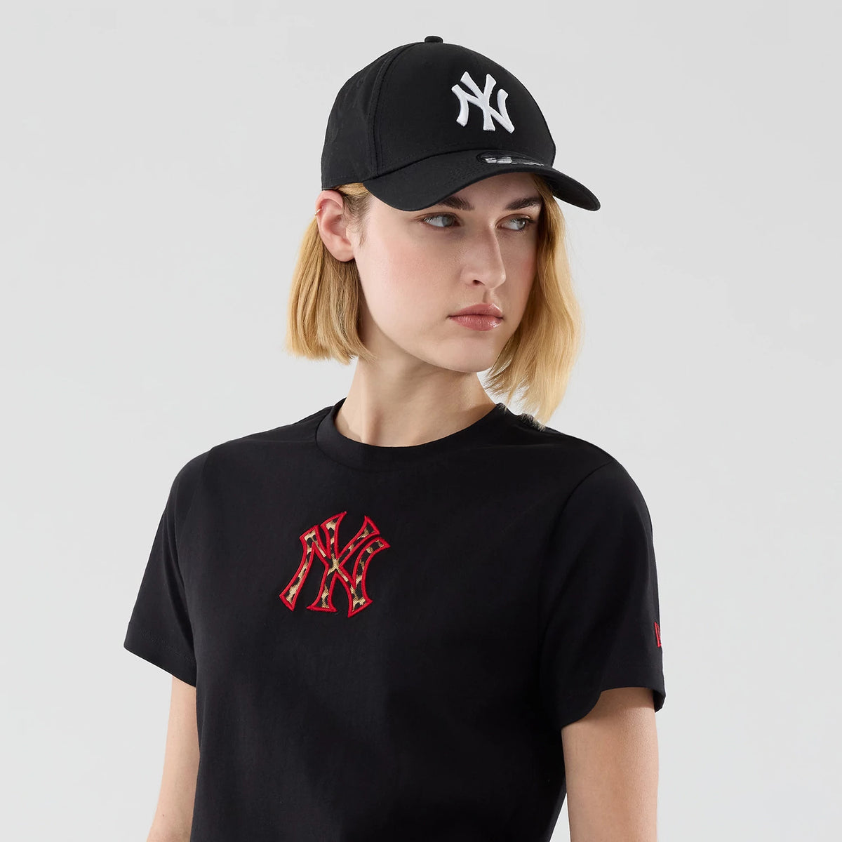 New Era New York Yankees Womens MLB Infill Black T-shirt, front view on-model showing a red infill New York Yankees logo embroidered on the chest, styled with a black cap featuring a white embroidered Yankees logo on the front crown.