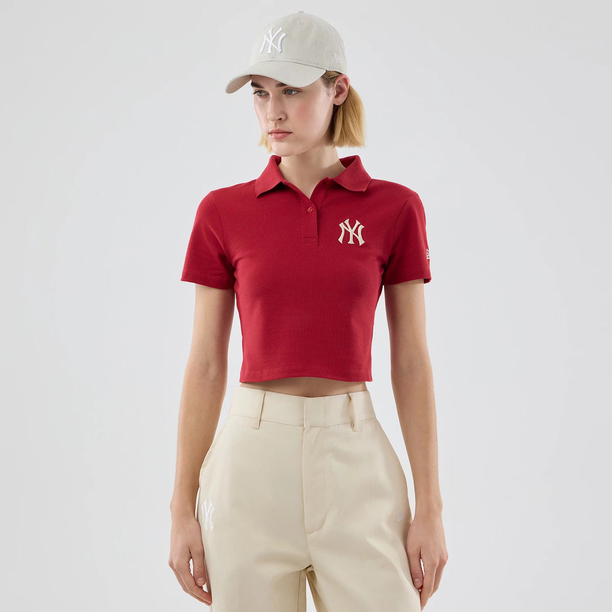 New Era New York Yankees Womens MLB Dark Red Cropped Slim Polo T-shirt, front view showing the white embroidered NY logo on the left chest of the dark red polo, styled on-model with light beige trousers and a matching cap.