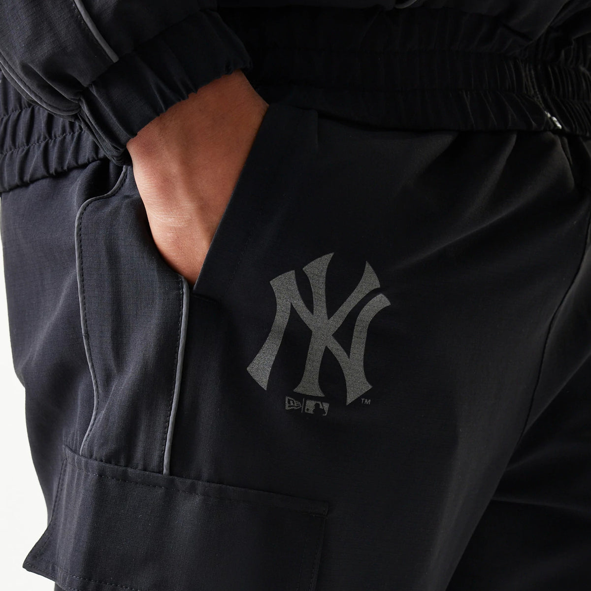 New Era New York Yankees MLB Utility Black Straight Leg Cargo Joggers, close-up view showing the grey printed NY logo on the right thigh with a hand in the side pocket and elastic waistband details.