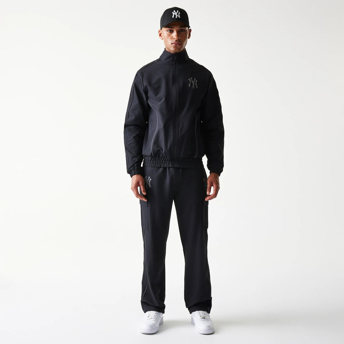 New Era New York Yankees MLB Utility Black Straight Leg Cargo Joggers, front view on a model wearing a matching jacket and cap, showing black joggers with side cargo pockets and Yankees logo on the upper left thigh.