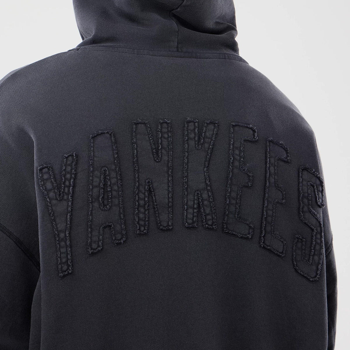 New Era New York Yankees MLB Washed Black Full Zip Hoodie, back view showing the textured black embroidered Yankees lettering across the upper back of the washed black fabric with a hood resting flat.