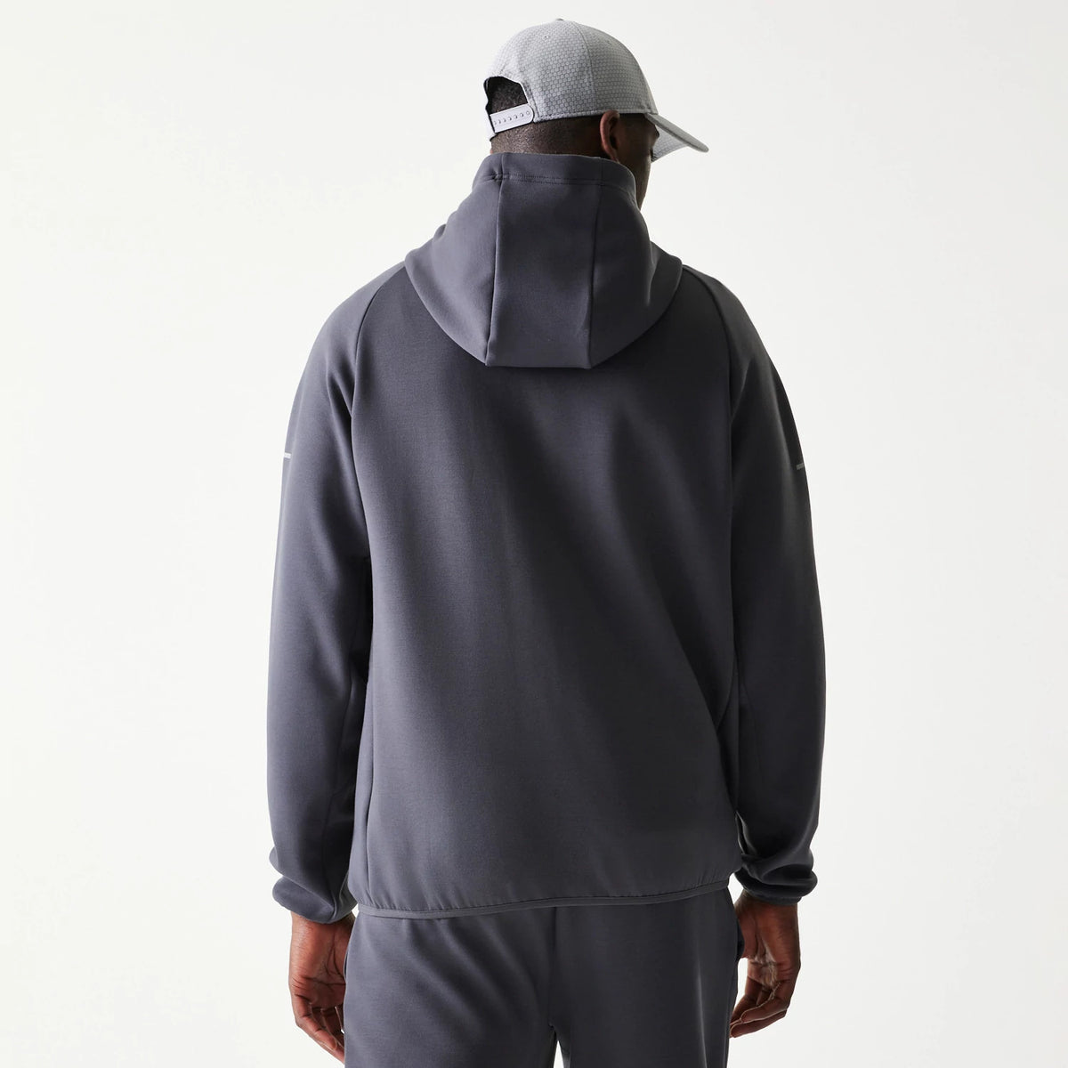 New Era New York Yankees MLB Dark Grey Full Zip Hoodie, back view on a model showcasing the plain dark grey design with a relaxed hood, no graphics and complemented with matching dark grey trousers and a light grey cap.