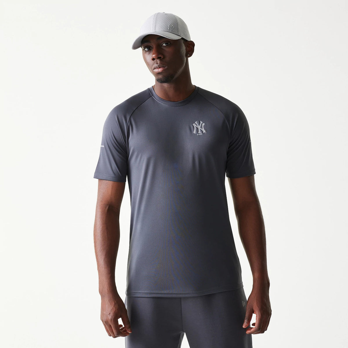 New Era New York Yankees MLB Dark Grey T-Shirt, front view on a model paired with a light grey cap, featuring a raised NY Yankees logo on the left chest and a dark grey finish with short sleeves.
