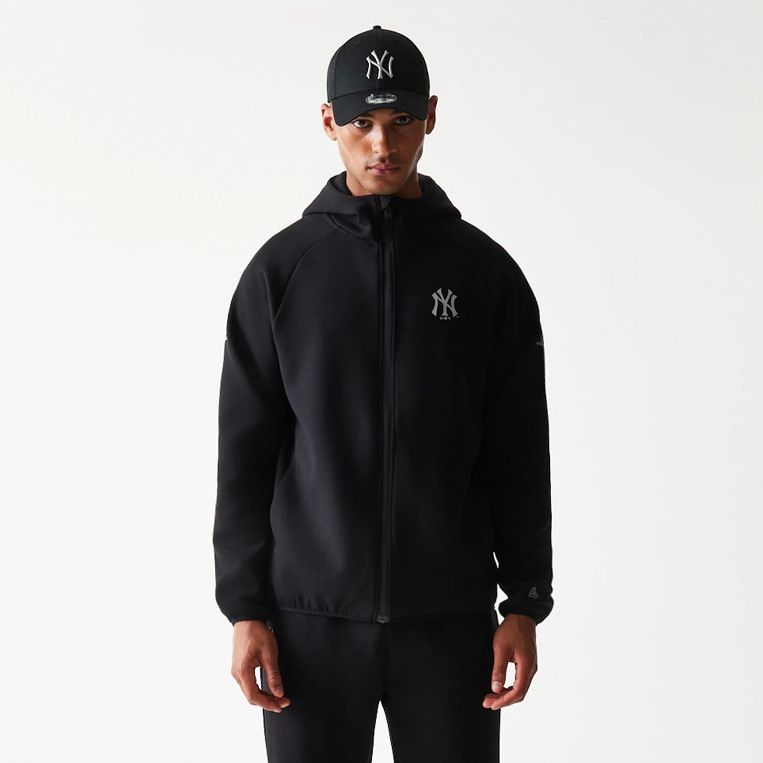 New Era New York Yankees MLB Black Full Zip Hoodie, front view on-model showcasing the black hoodie with a full zip closure, featuring an embroidered New York Yankees logo on the left chest and a hood covering the back of the neck.