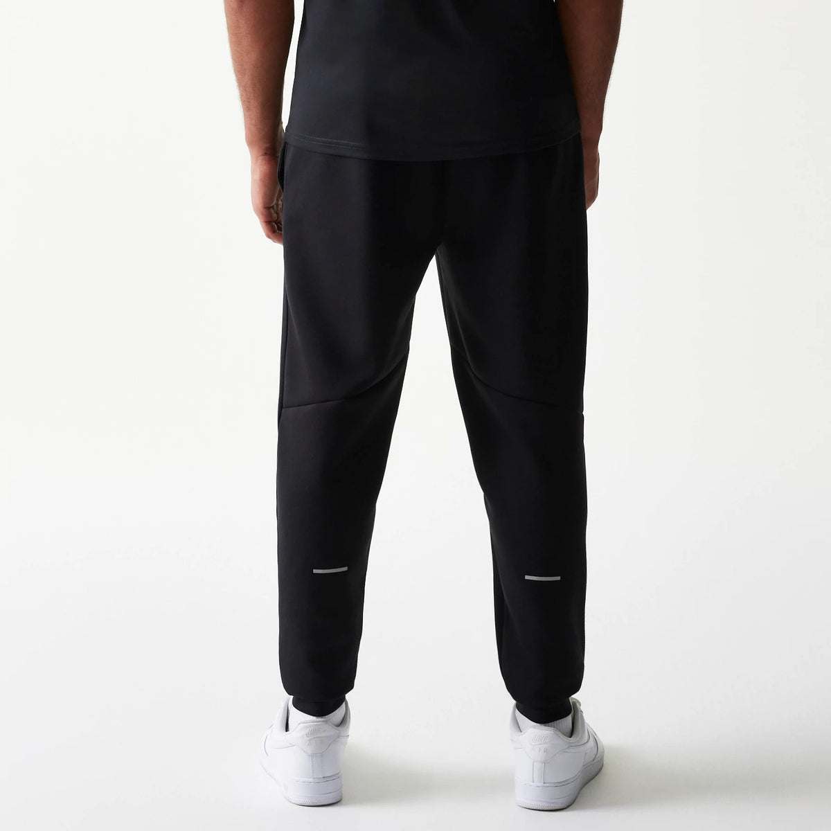 New Era New York Yankees MLB Black Joggers, rear view showing a relaxed fit with seam on the legs, and small reflective accents near the cuffs, worn with white trainers against a plain background.