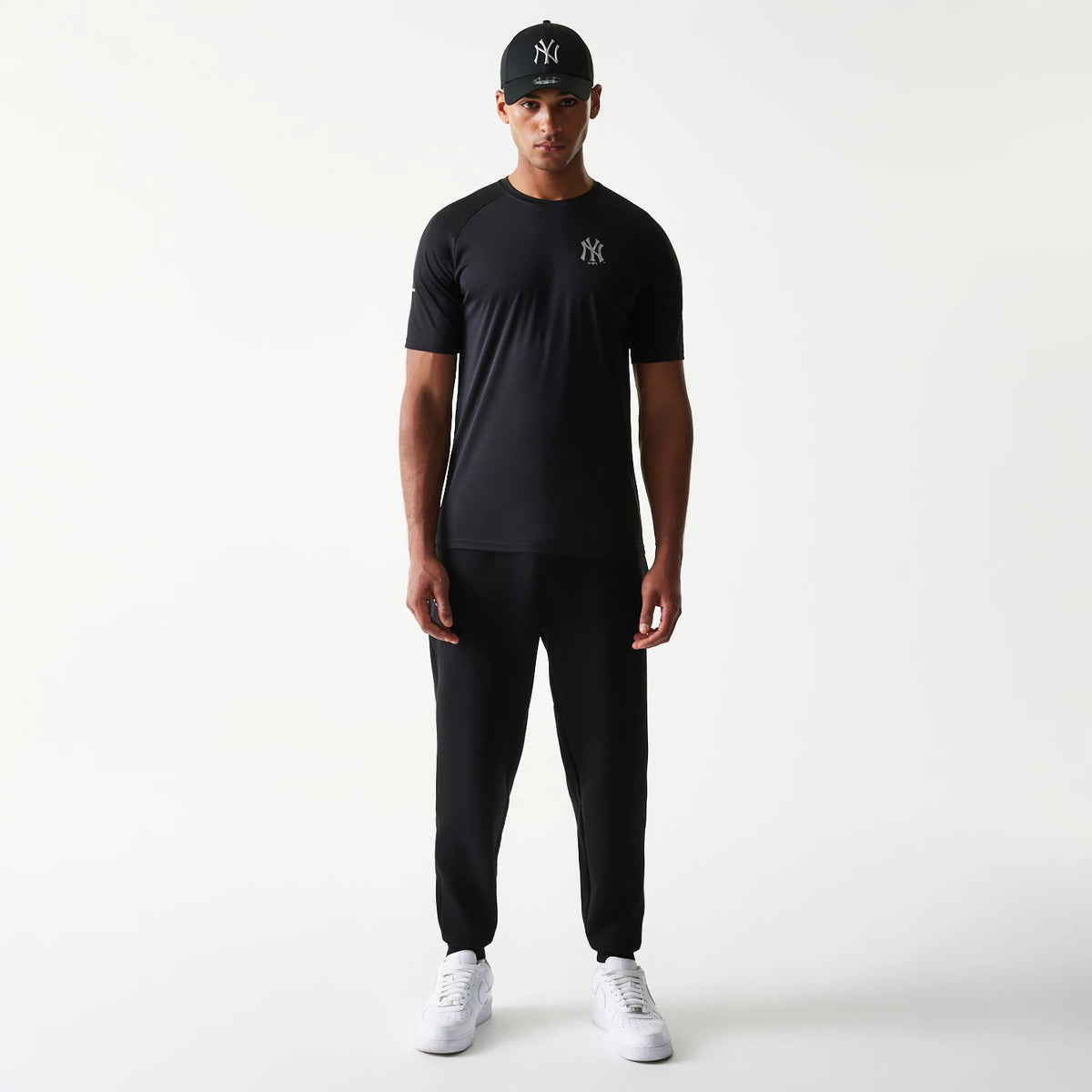 New Era New York Yankees MLB Black Joggers, front view on a model with a matching black New York Yankees cap and T-shirt, showing elasticated cuffs and a relaxed fit, paired with white trainers.