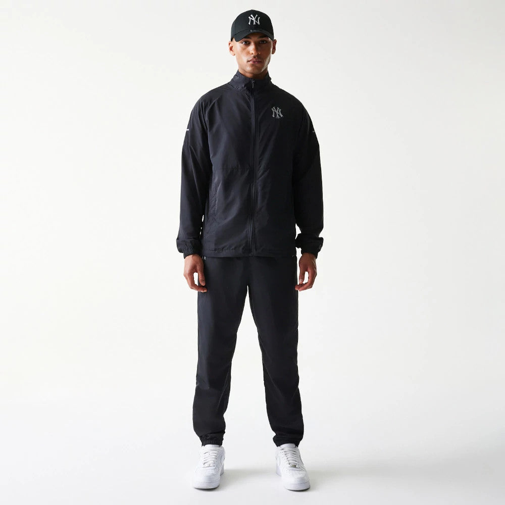 New Era New York Yankees MLB Reflective Logo Black Track Pants, front view on a model with a matching black jacket and cap, featuring an elastic waistband and ankle cuffs, paired with white trainers for a look.