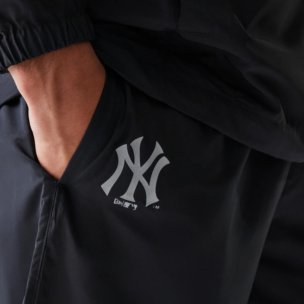 New Era New York Yankees MLB Reflective Logo Black Track Pants, close-up showing the silver reflective NY logo on the left thigh, with the model's hand in the side pocket, highlighting the black fabric and elasticated cuff.