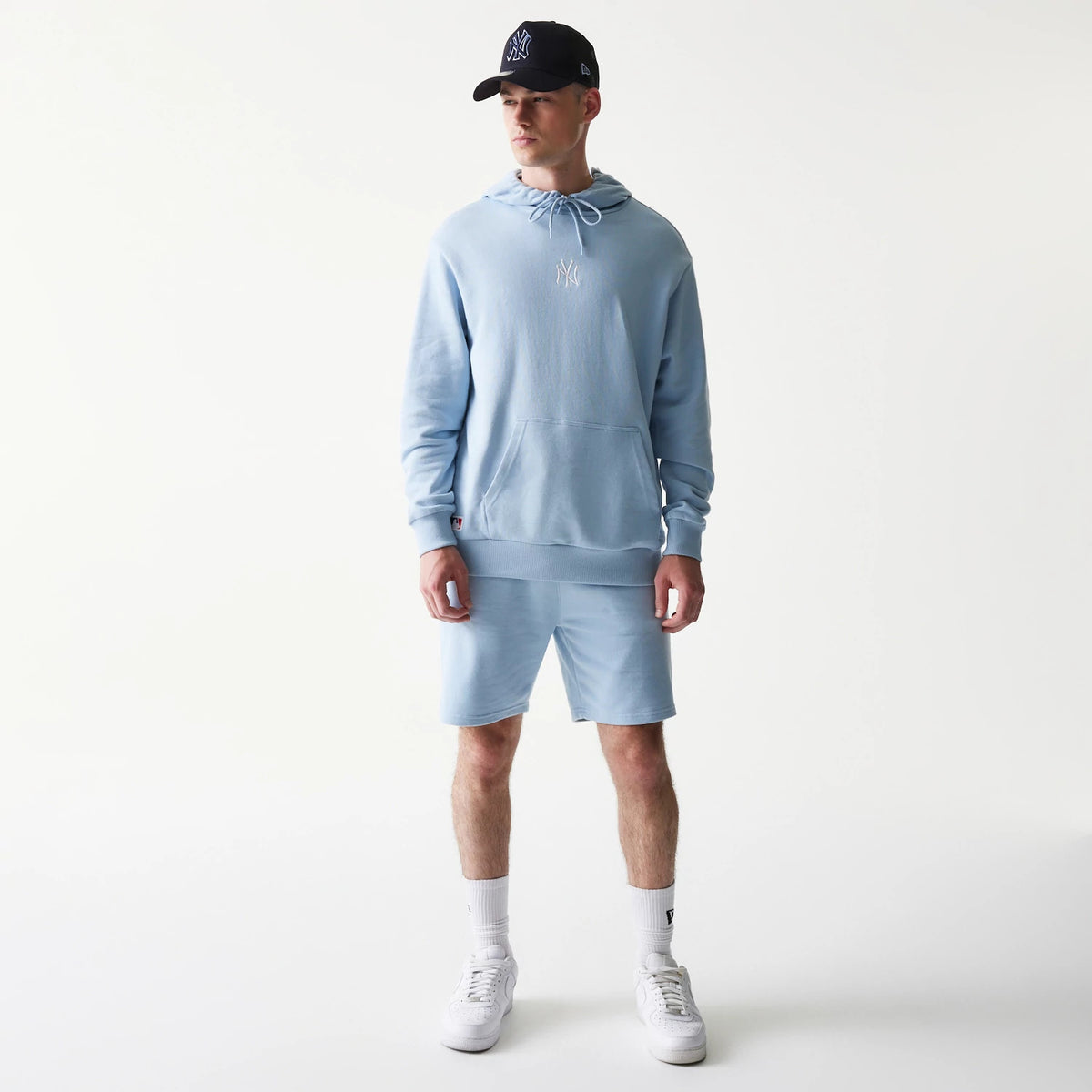 New Era New York Yankees MLB Midi Pastel Blue Oversized Pullover Hoodie, front view on a model showing the pastel blue hoodie with a white embroidered Yankees logo on the chest, styled with matching shorts and a black Yankees cap.