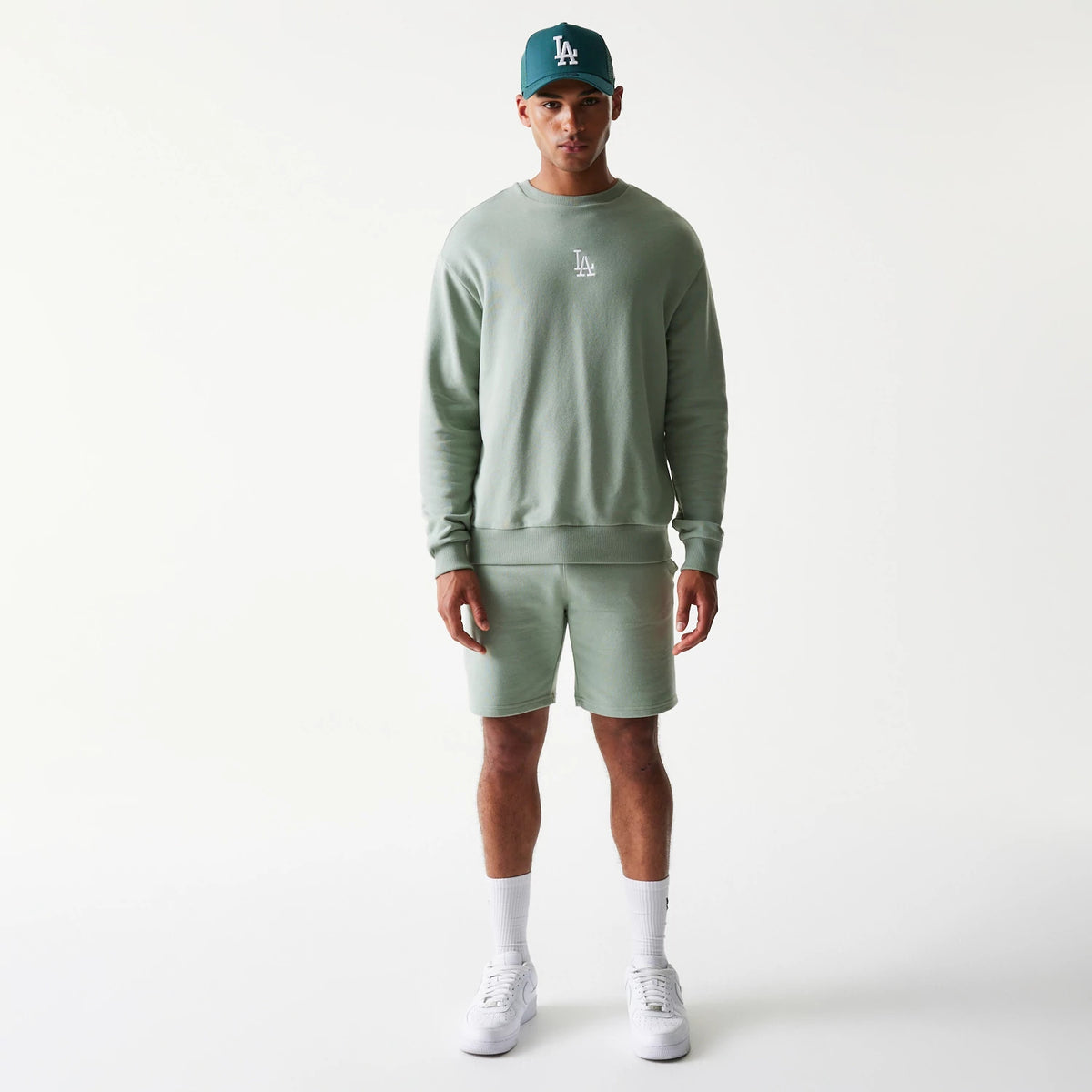 New Era LA Dodgers MLB Midi Green Oversized Crew Neck Sweater, front view on a model wearing a matching cap, showing the white embroidered LA logo on the chest and relaxed fit of the green fabric.
