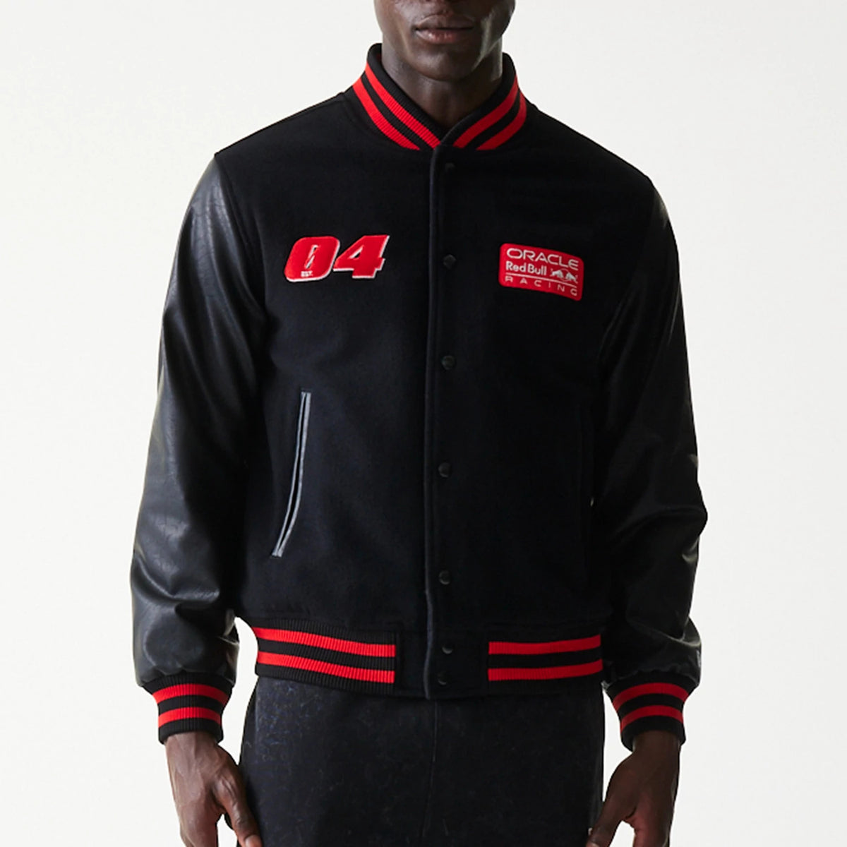 New Era Red Bull Racing Black Varsity Jacket, front view showing a varsity-style jacket on model with red embroidered number 04 and Oracle Red Bull Racing patch on chest, red striped cuffs, collar, and hem.
