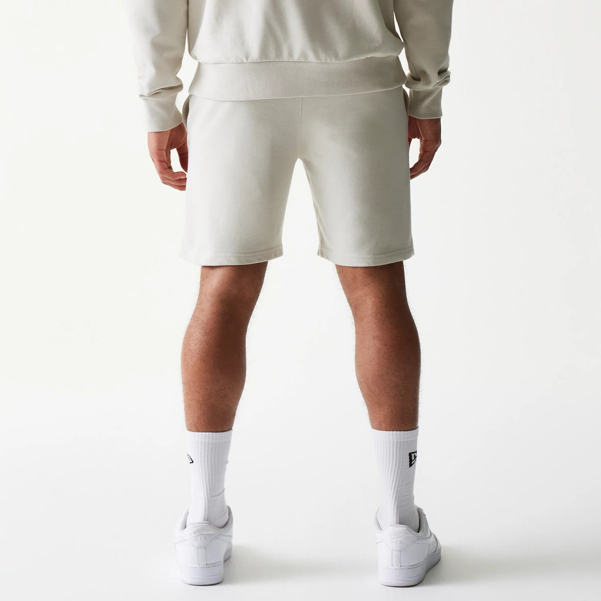 New Era LA Lakers NBA League Essential Light Beige Shorts, back view on-model showing a clean design with no logos or graphics, styled casually with a matching light top and white trainers.