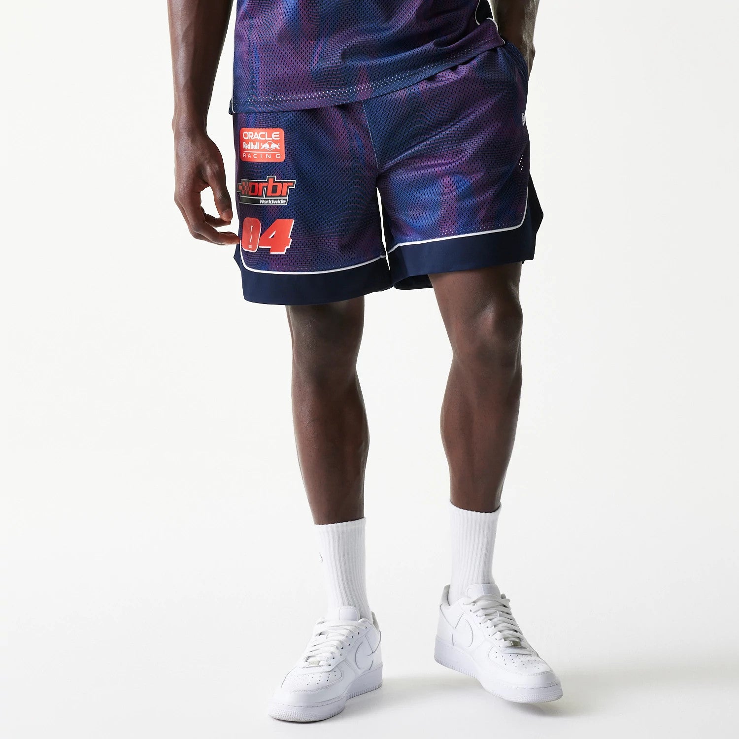 New Era Red Bull Racing Dark Blue Oversized Mesh Shorts, front view on a model, displaying a dark blue and purple mesh design with printed sponsor logos on the left leg above the number 04 and navy blue trim at the hem.