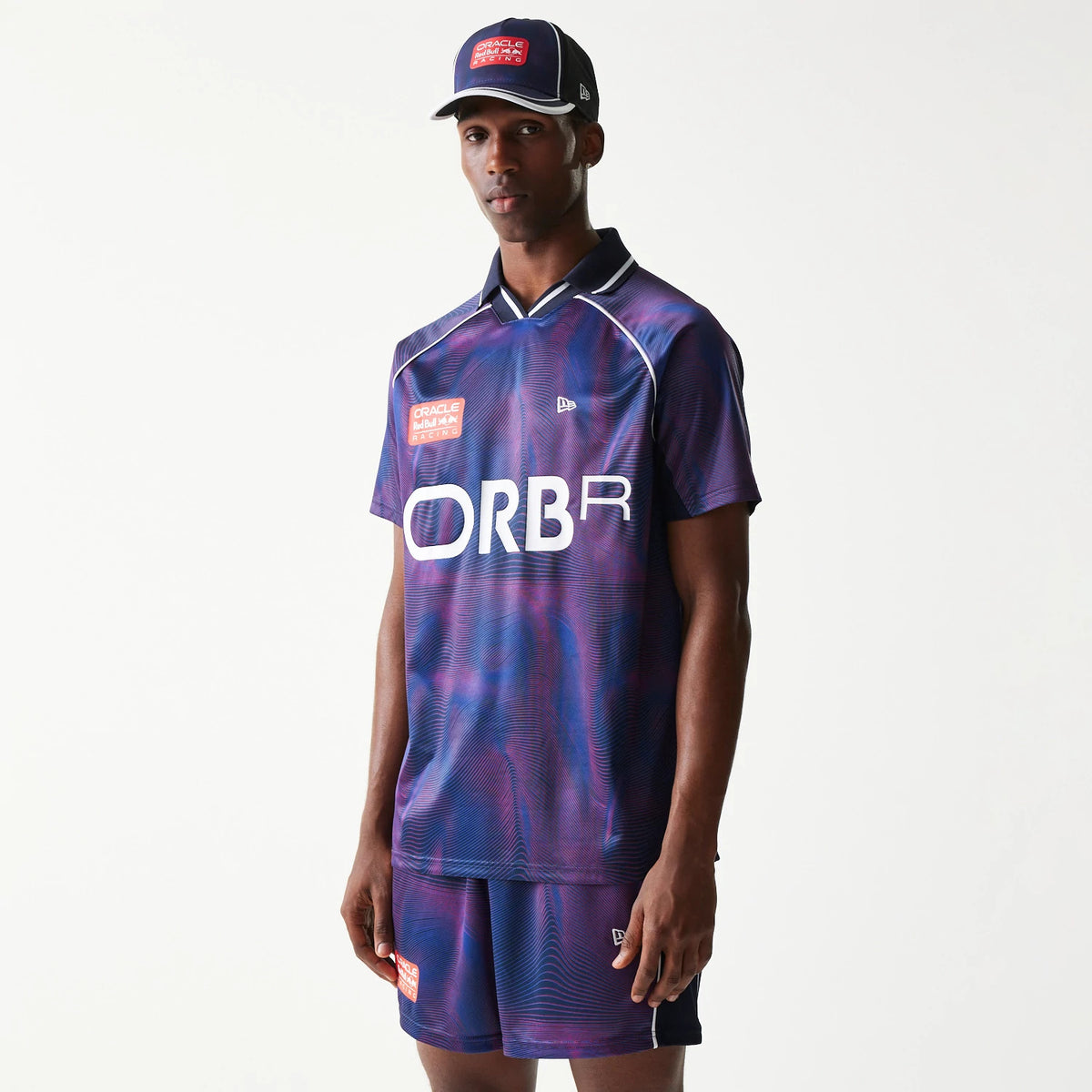 New Era Red Bull Racing All Over Print Dark Blue Football T-Shirt, front three-quarter view on-model showing the swirl pattern with a printed team logo on the chest, a small raised New Era logo on the right, and styled with matching shorts and cap.