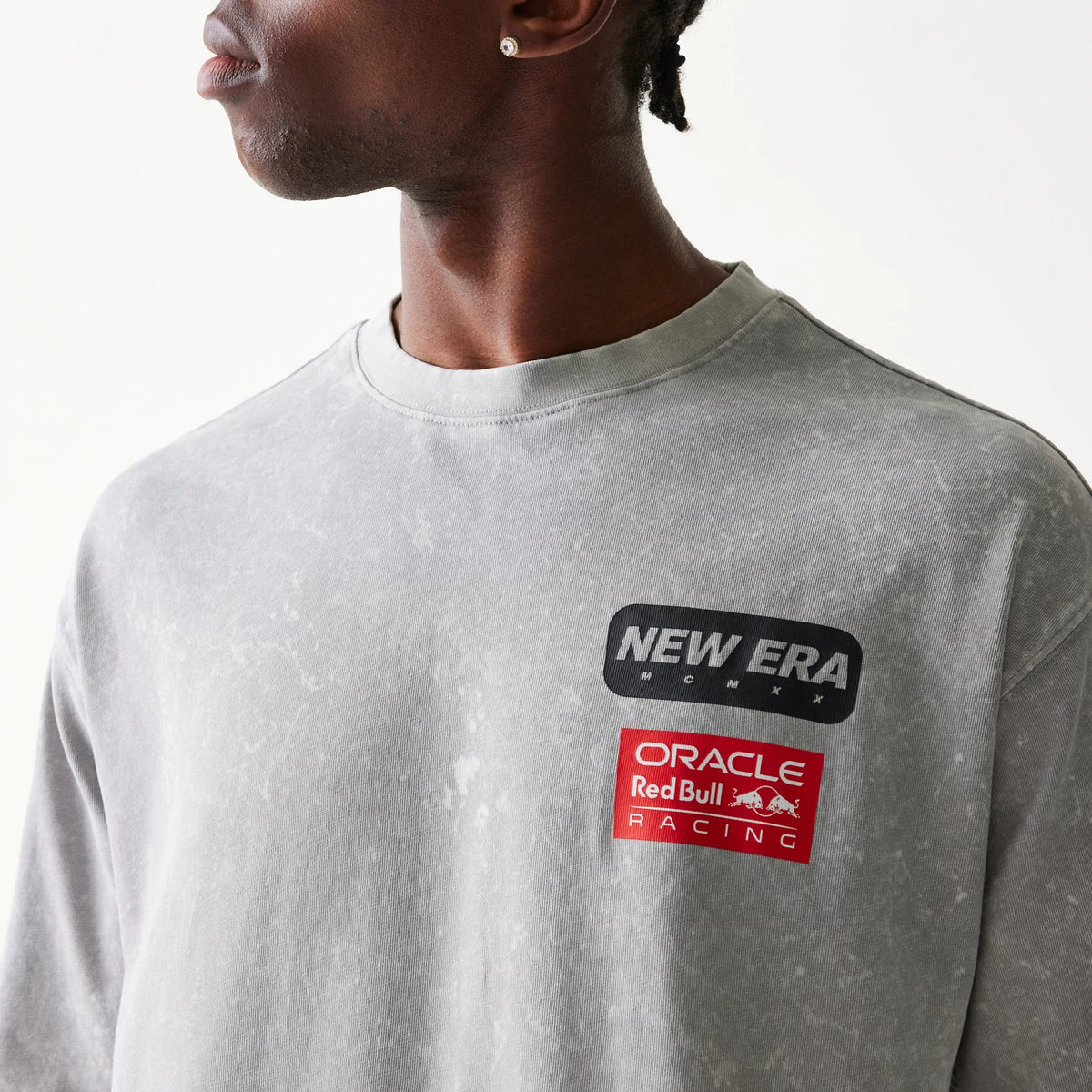 New Era Red Bull Racing Linear Graphic Grey Oversized T-Shirt, front view on-model showing a large printed New Era logo in black near the shoulder and a red Oracle Red Bull Racing logo below it on a washed grey background.