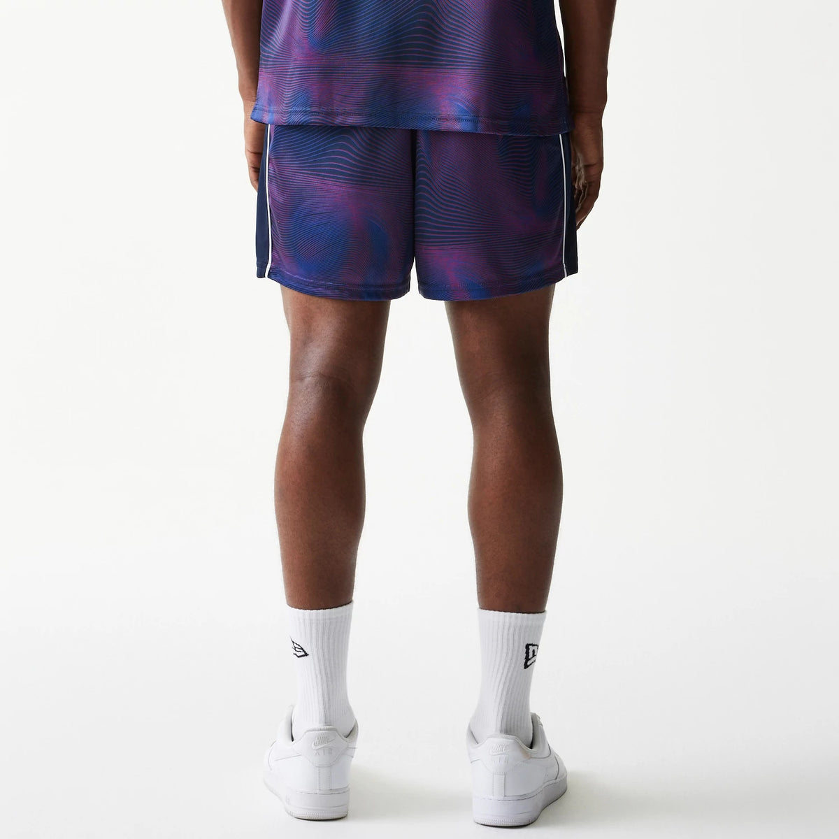 New Era Red Bull Racing All Over Print Dark Blue Football Shorts, back view showing a swirling purple and dark blue pattern with vertical stripes on the sides, styled on a model with matching socks and trainers.
