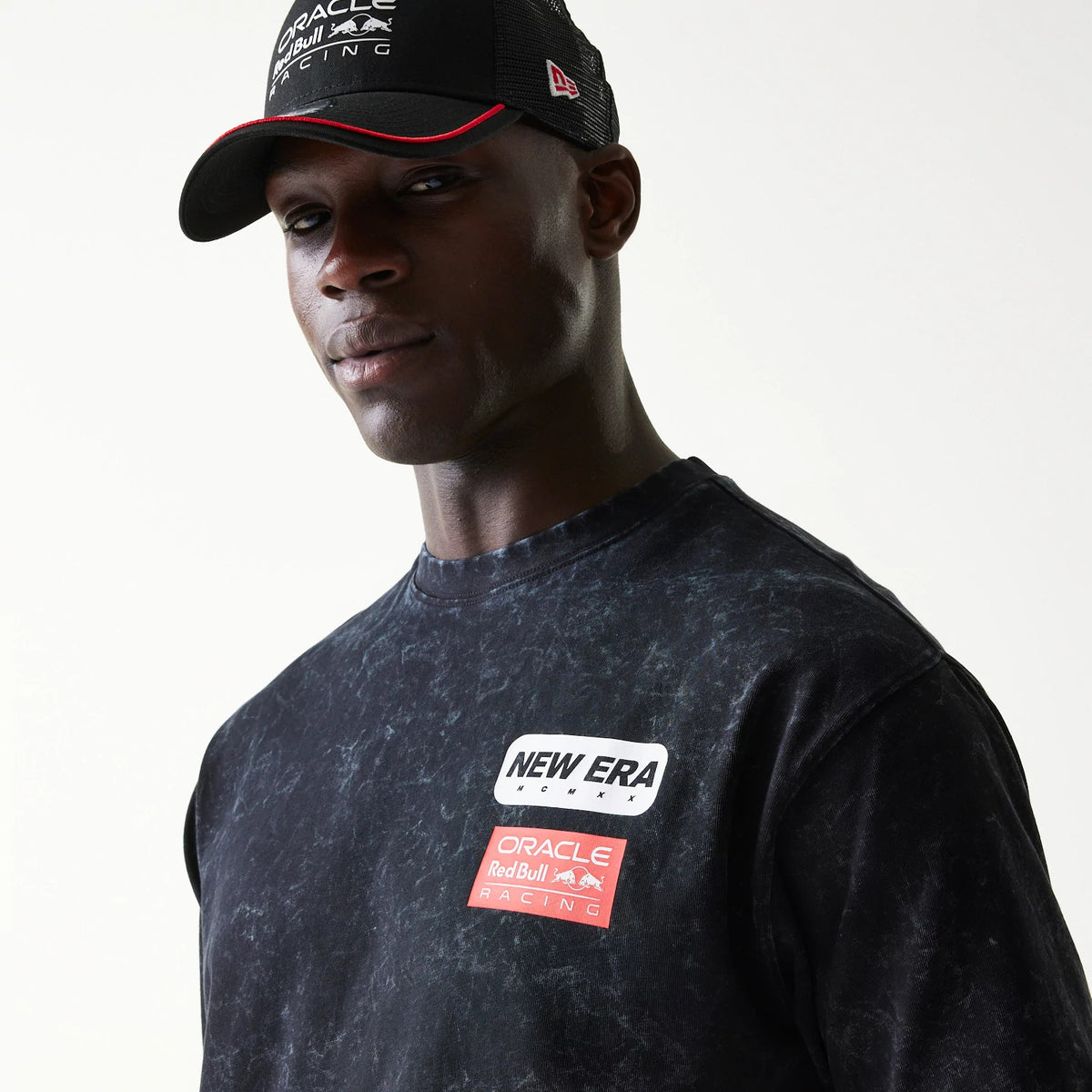 New Era Red Bull Racing Linear Graphic Black Oversized T-Shirt, front view on-model showing a printed New Era logo in white next to a red Oracle Red Bull Racing graphic on the marbled black fabric.