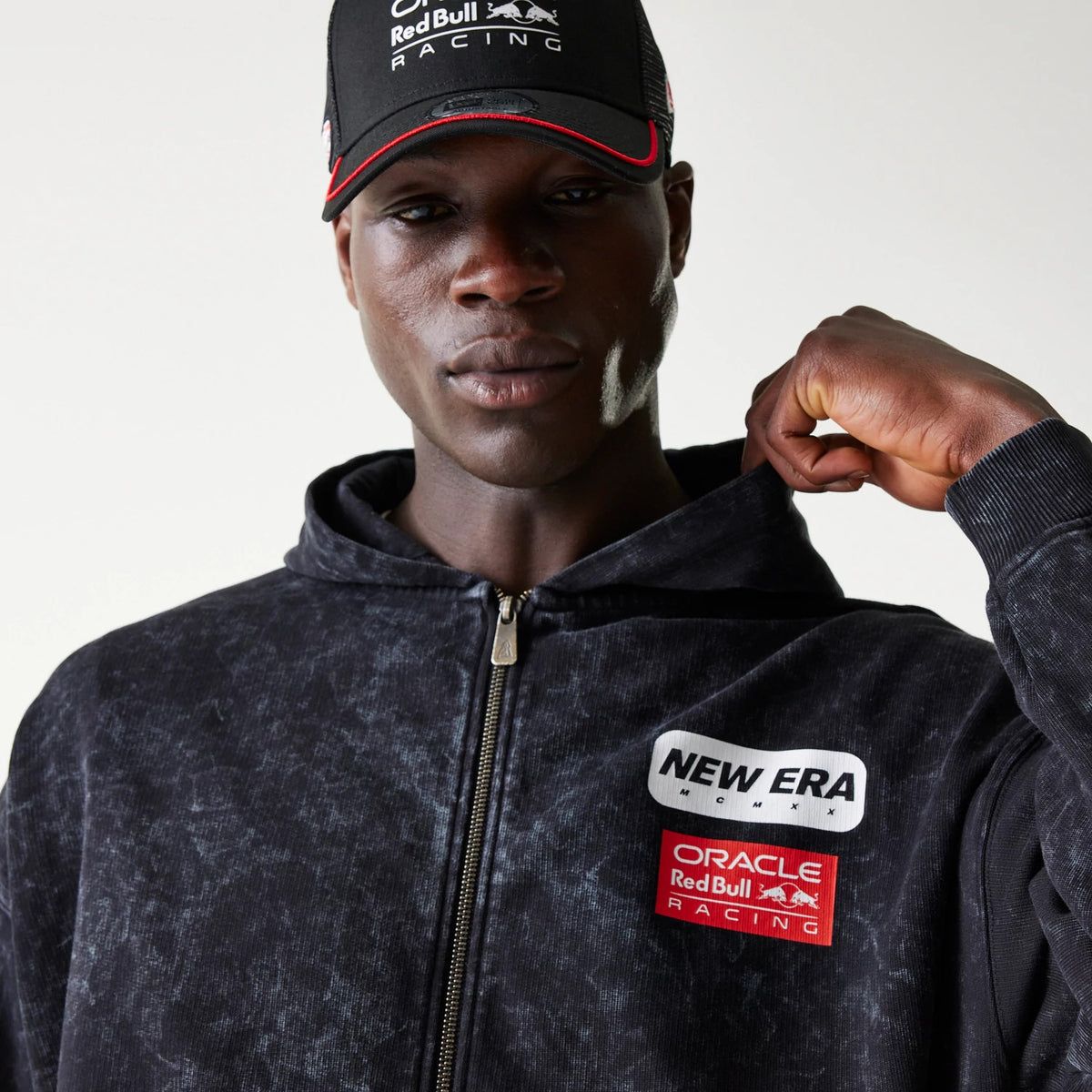 New Era Red Bull Racing Dropped Shoulder Black Dropped Shoulder Full Zip Hoodie, front view on-model featuring a full zip, a New Era embroidered logo on the chest, and a Red Bull Racing patch below it on a black patterned hoodie.