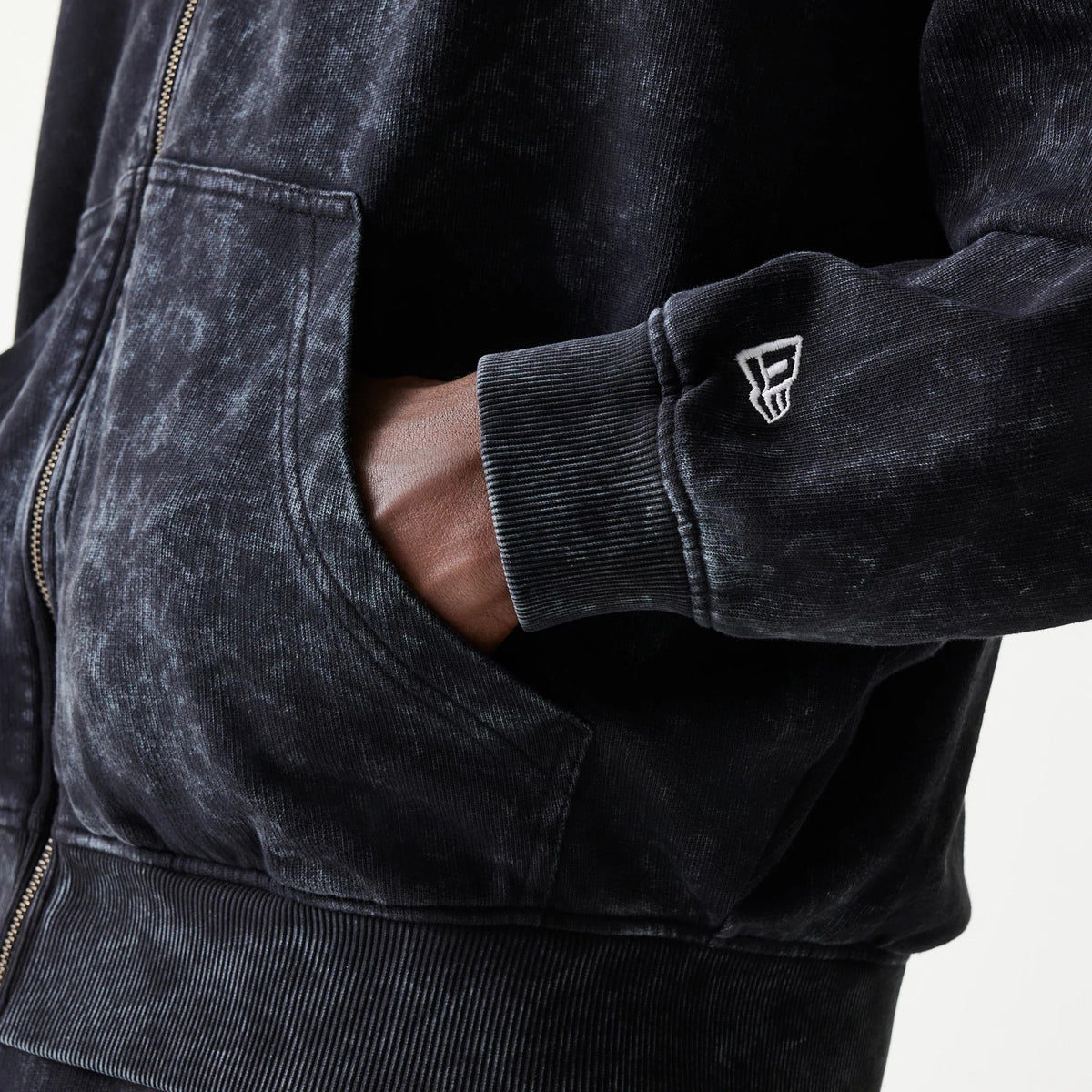 New Era Red Bull Racing Graphic Black Dropped Shoulder Full Zip Hoodie, side view showing a hand in the front pocket and an embroidered logo on the sleeve cuff above a ribbed hem and faded black fabric.