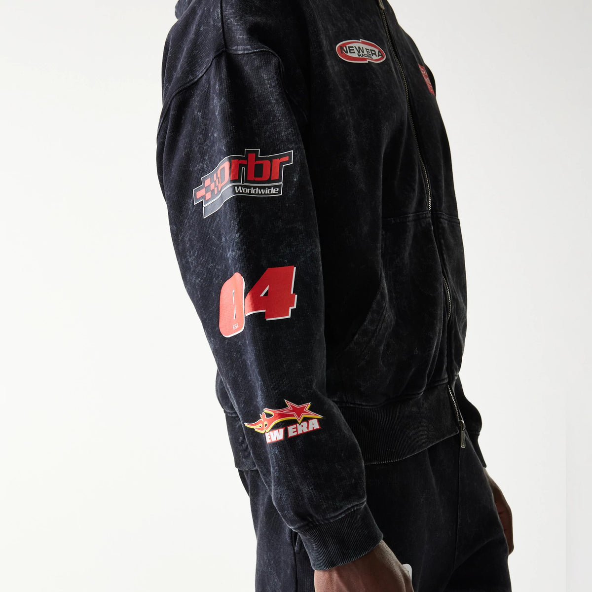 New Era Red Bull Racing Graphic Black Dropped Shoulder Full Zip Hoodie, side view on-model showing the RBR Worldwide and number 04 graphics on the sleeve, a printed New Era logo near the ribbed cuff, and a zip closure along the front.
