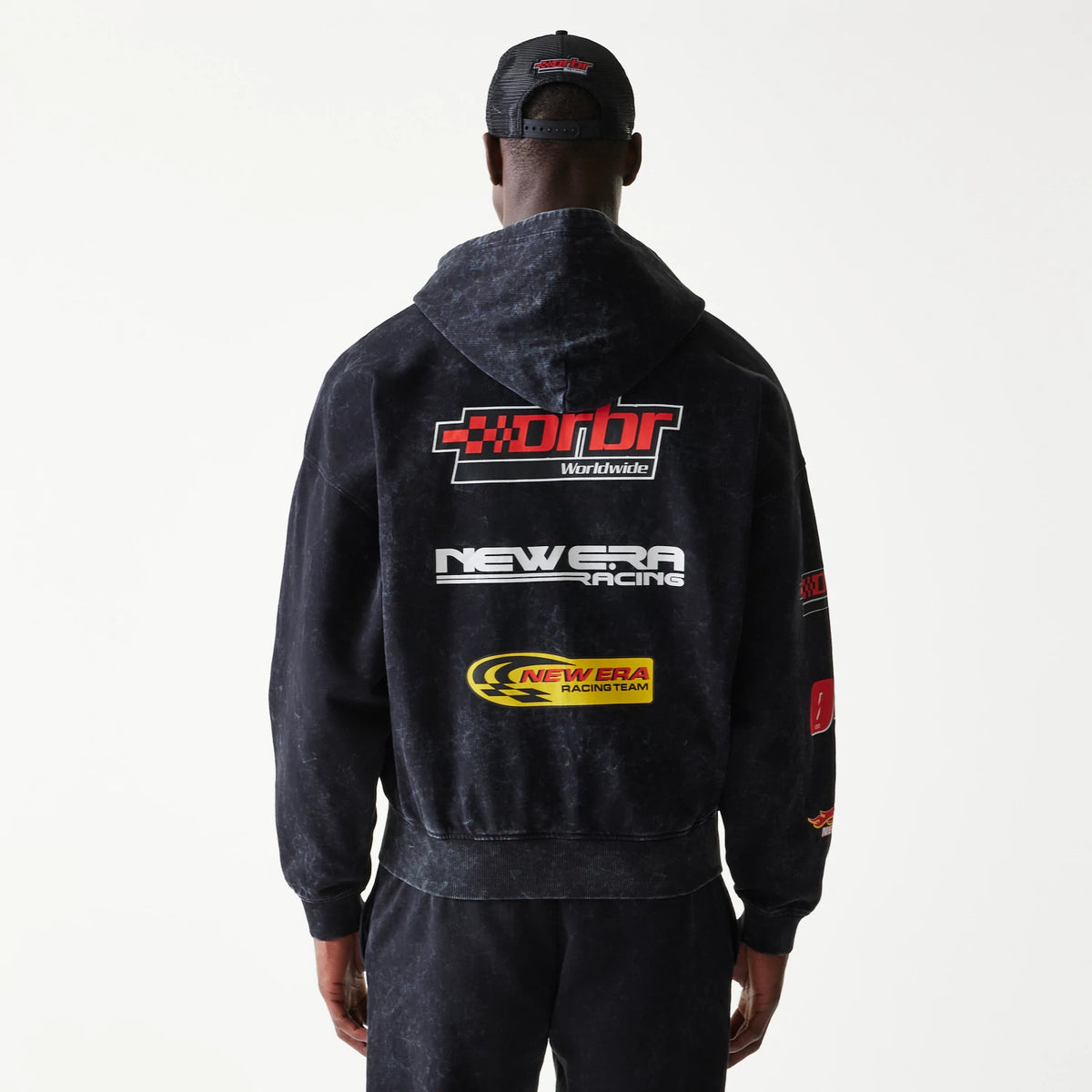 New Era Red Bull Racing Graphic Black Dropped Shoulder Full Zip Hoodie, back view on-model showing racing-themed graphics and lettering across the back, including red drbr Worldwide and white New Era Racing logos.