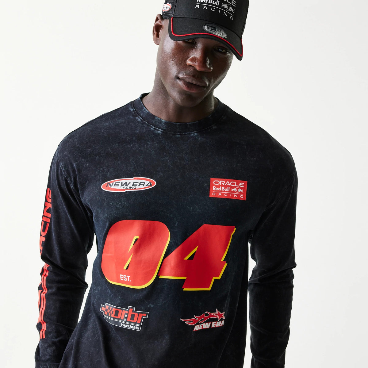 New Era Red Bull Racing Graphic Black Long Sleeve T-Shirt, front view on-model showing red 04 est. graphic on the chest, New Era and Oracle Racing logos above, and red Racing lettering down the right sleeve.