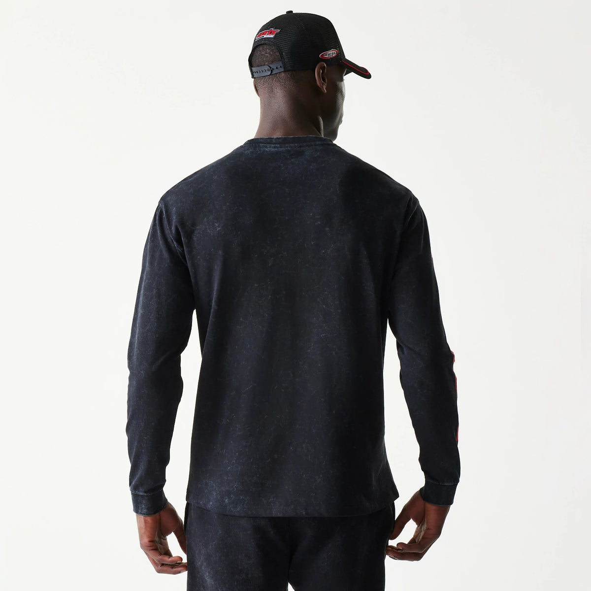 New Era Red Bull Racing Graphic Black Long Sleeve T-Shirt, back view on a model paired with a matching cap, featuring a marbled texture on the black fabric and a clean silhouette, with the sleeves extending to the wrists.