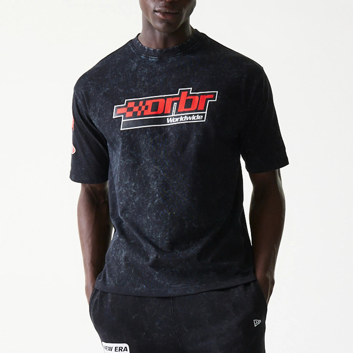 New Era Red Bull Racing Graphic Black Oversized T-Shirt, front view on a model showing a red rbr Worldwide graphic printed across the chest on a textured black background, with short sleeves and relaxed fit styling.