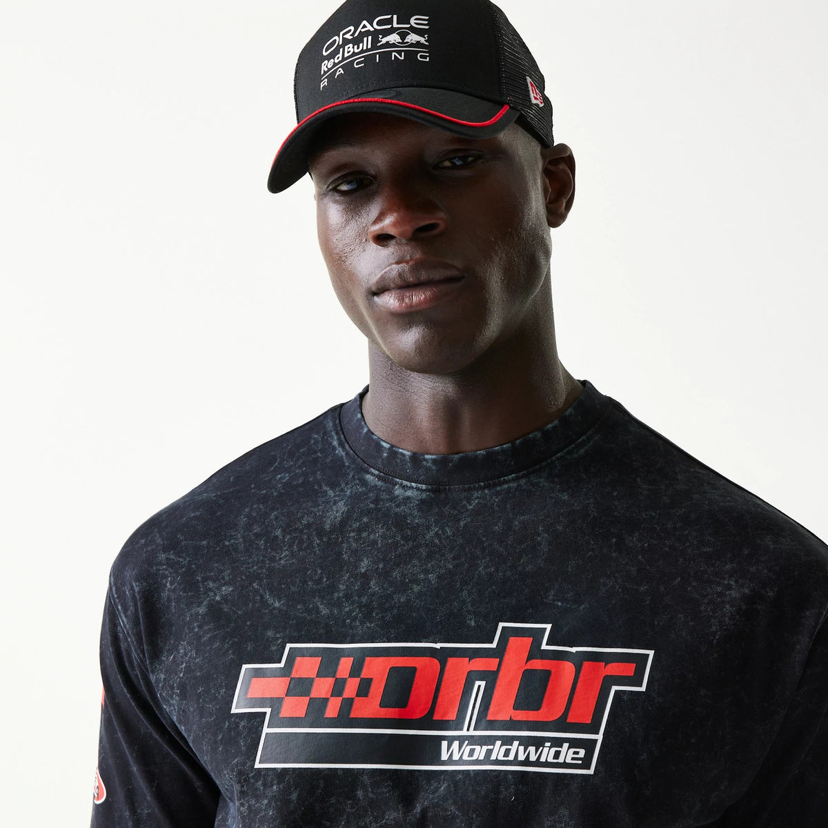 New Era Red Bull Racing Graphic Black Oversized T-Shirt, front view on-model displaying a red and white printed rbr Worldwide graphic across the chest, paired with a black cap featuring an embroidered Red Bull Racing logo.