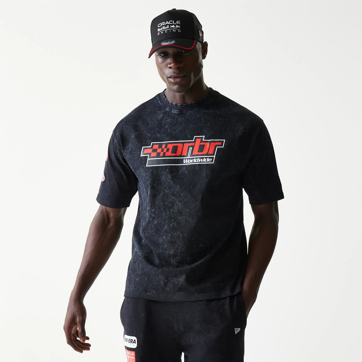 New Era Red Bull Racing Graphic Black Oversized T-Shirt, front view on-model showing a red and white chest graphic with drbr Worldwide text, complemented by a matching cap and casual styling.