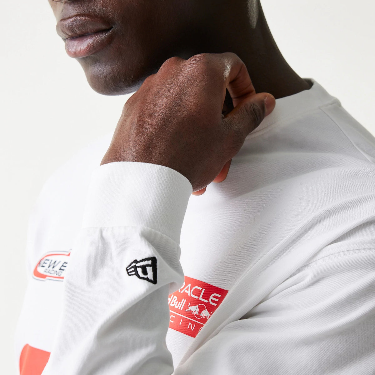 New Era Red Bull Racing Graphic White Long Sleeve T-Shirt, on-model view showing the New Era embroidered logo on the sleeve cuff and red racing graphics on the chest, with the model lightly touching the neck of the shirt.