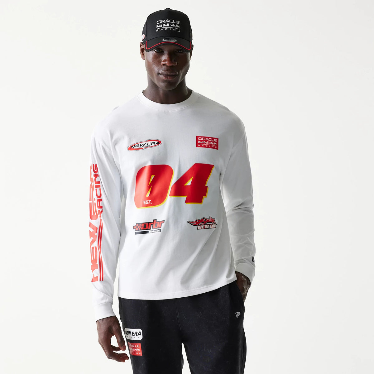 New Era Red Bull Racing Graphic White Long Sleeve T-Shirt, front view on-model showing red 04 and New Era logos on the chest, with further branded graphics on the sleeve and an embroidered cap logo worn above.