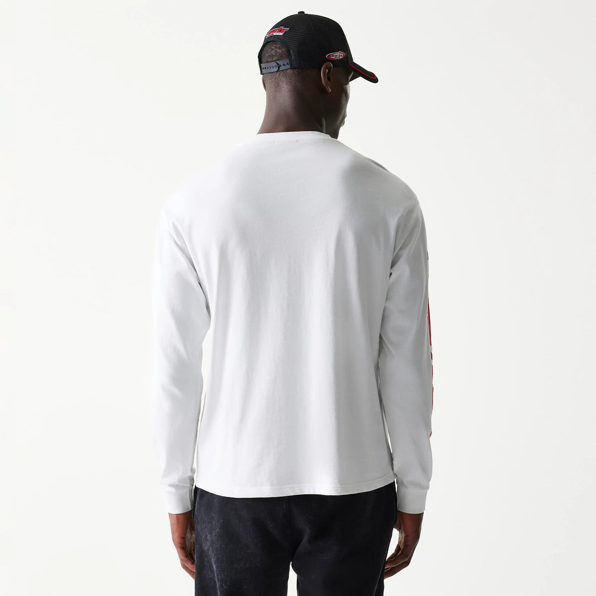 New Era Red Bull Racing Graphic White Long Sleeve T-Shirt, back view on a model displaying the plain white fabric with long sleeves, complemented by a black cap that features embroidered racing logos at the back.