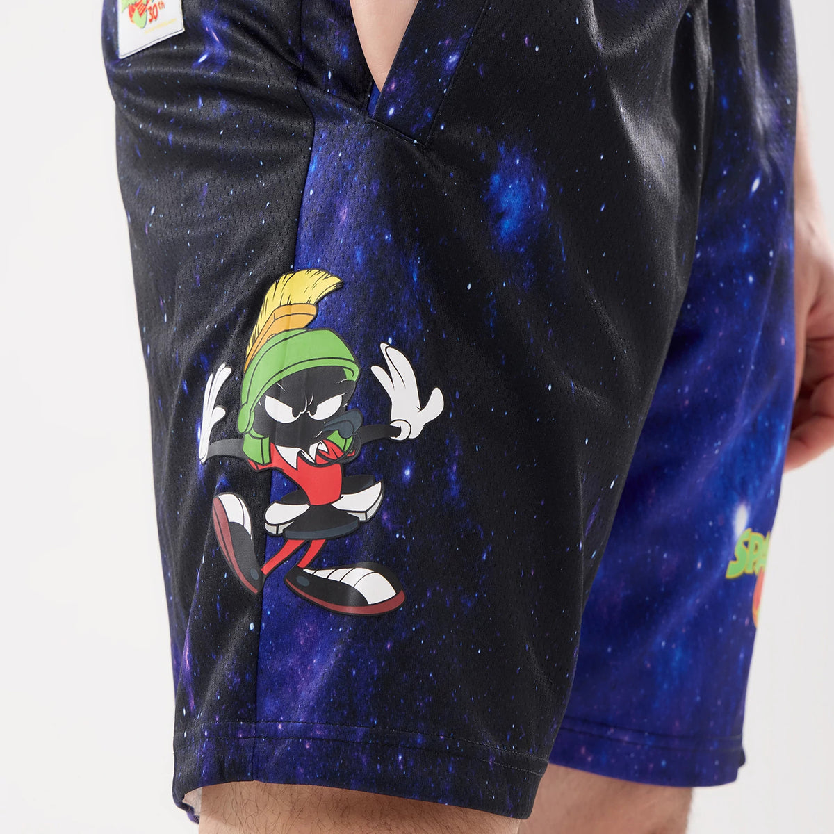 New Era Space Jam Warner Brothers Space Jam White Oversized Shorts, three-quarter view showing a graphic of Marvin the Martian on a space-themed dark background and an embroidered Space Jam logo on the side near the hem.