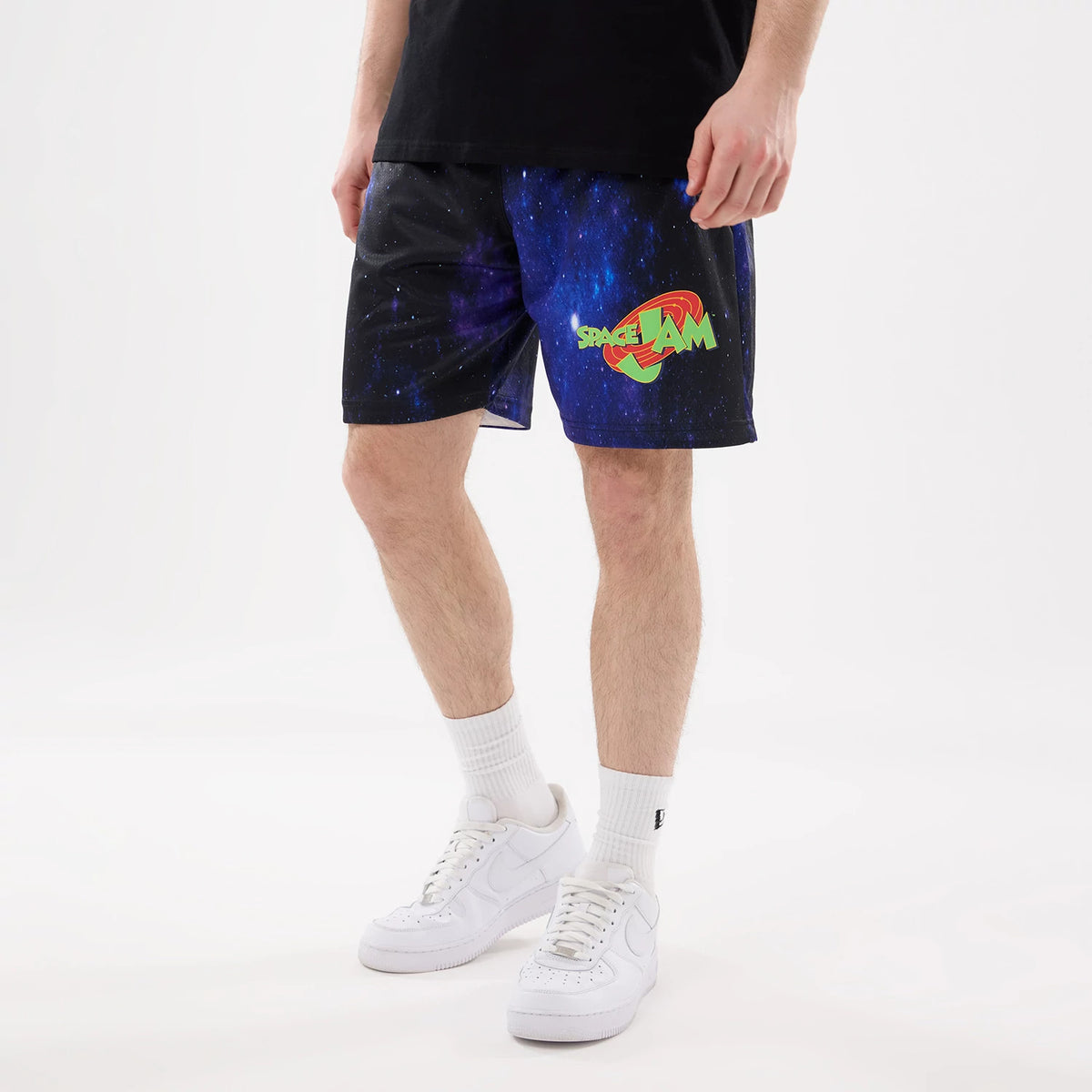 New Era Space Jam Warner Brothers Space Jam White Oversized Shorts, three-quarter view on-model showing a blue galaxy print with a large embroidered Space Jam logo on the left leg, styled with white trainers and socks.