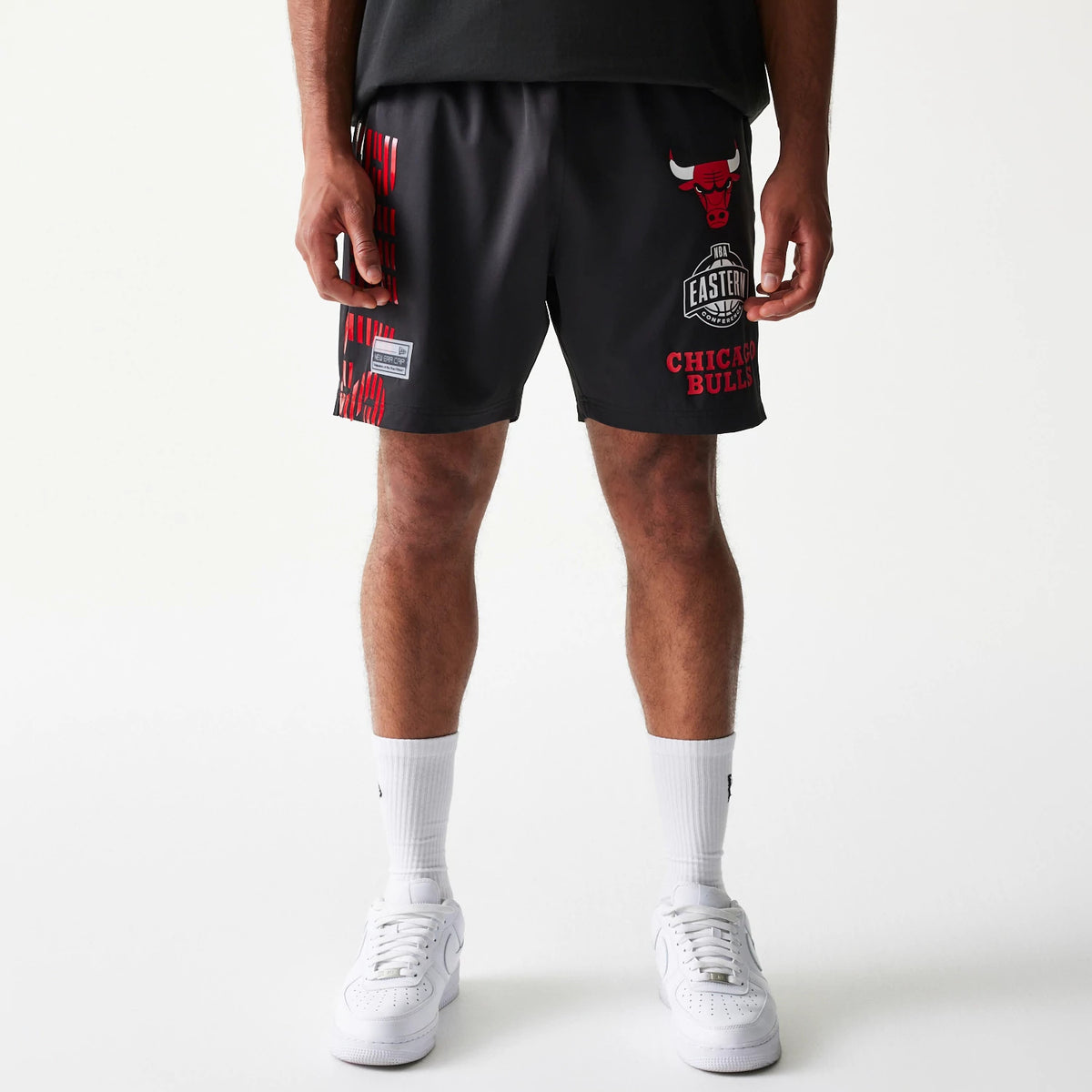 New Era Chicago Bulls NBA Match Black Oversized Shorts, front view on a model showing the red printed Chicago Bulls logo and text on the right leg, NBA Eastern logo below, and vertical red stripes on the left leg.