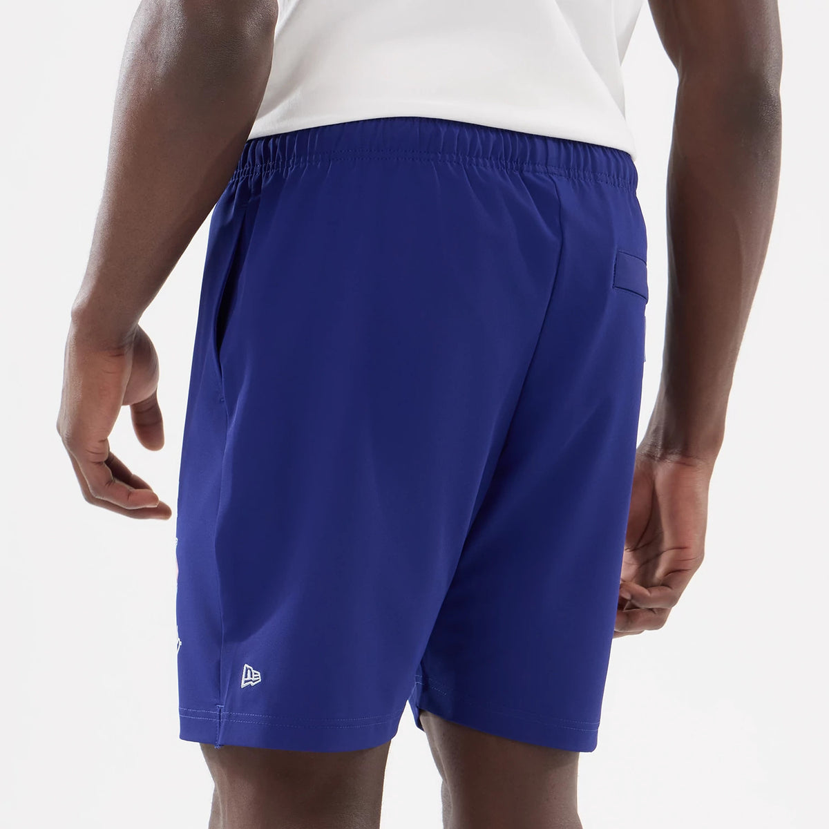 New Era LA Dodgers MLB Match Dark Blue Oversized Shorts, back view on-model showing the elastic waistband, a single back pocket, and a white embroidered New Era logo above the hem on the left leg.