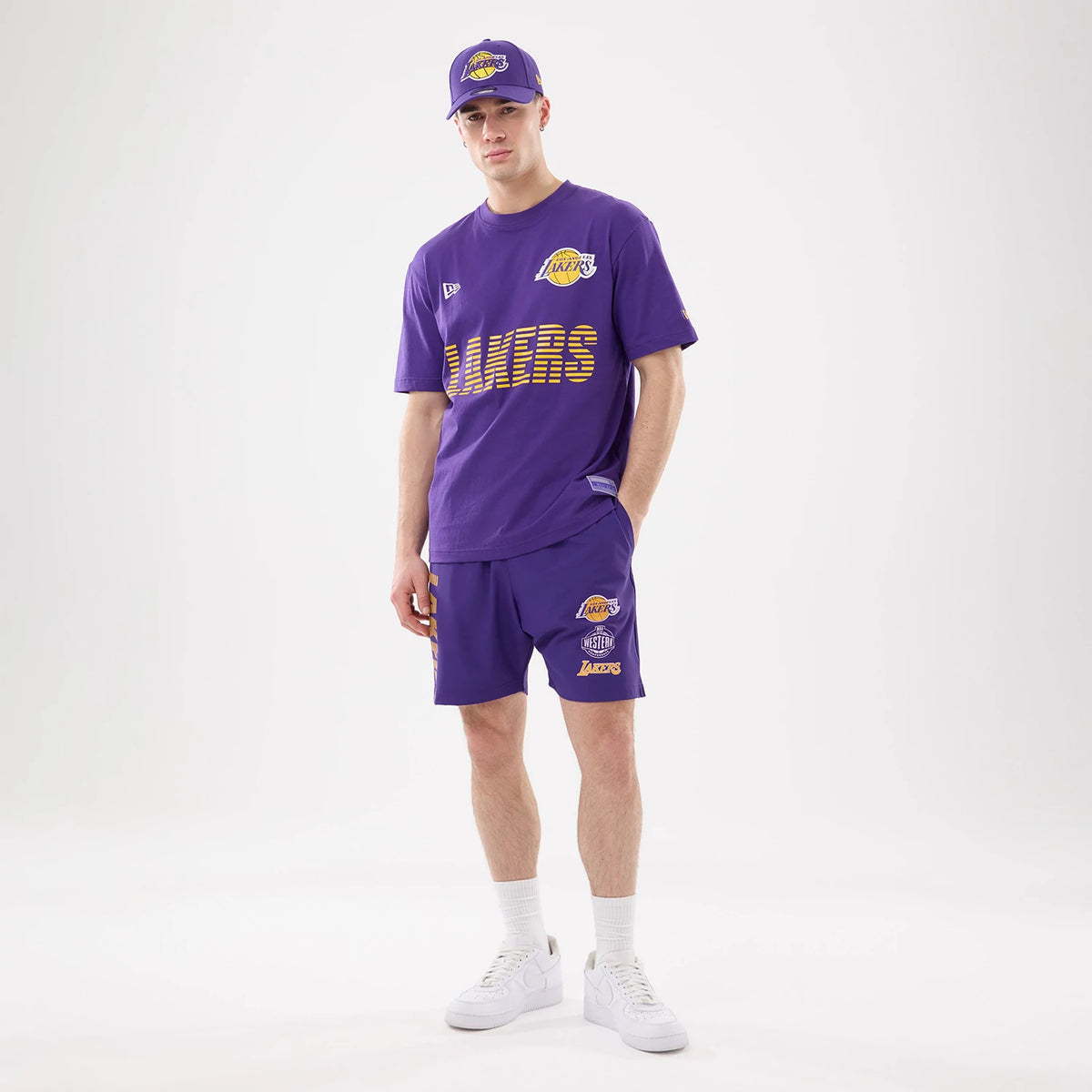New Era LA Lakers NBA Match Purple Oversized Shorts, on-model view showing the embroidered Lakers logo on the right leg and matching T-shirt with Lakers lettering, styled with white trainers and socks.