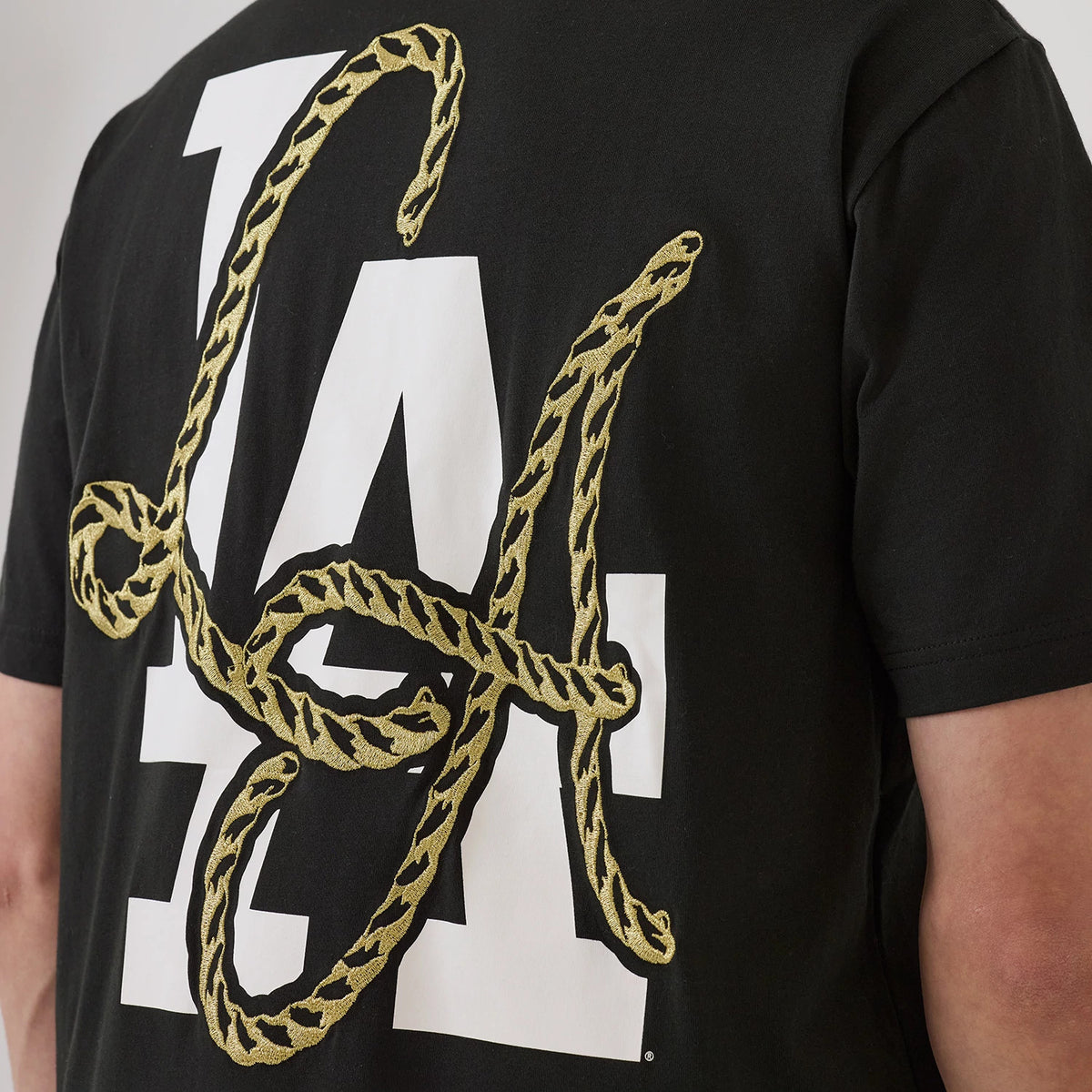 New Era LA Dodgers MLB Cowboy Graphic Black T-Shirt, back view showing large white LA lettering with an embroidered gold rope design overlaying the letters, set against the black fabric of the t-shirt.