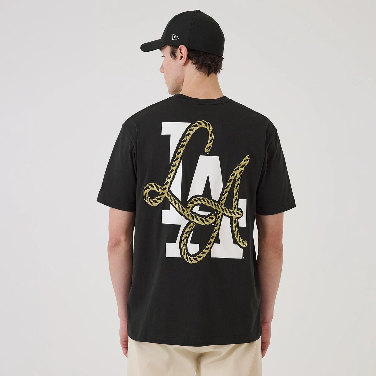 New Era LA Dodgers MLB Cowboy Graphic Black T-Shirt, back view on a model showing a white LA logo entwined with a gold rope graphic on the black fabric, paired with a black cap featuring an embroidered New Era logo.